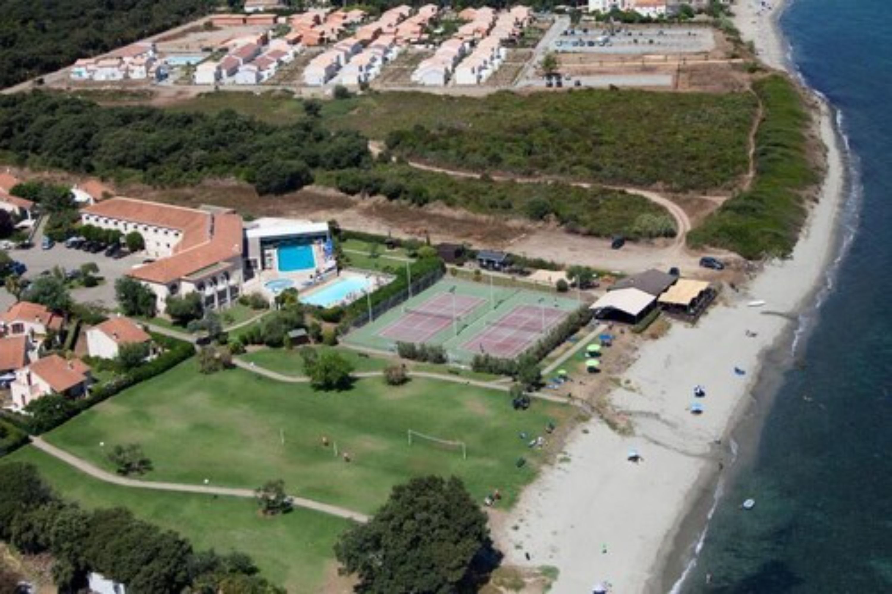 Vista aérea de una zona residencial costera con casas, una cancha de tenis y una playa.
