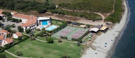 Vista aérea de una zona residencial costera con casas, una cancha de tenis y una playa.