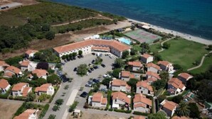 An aerial view of a coastal residential area with houses, a parking lot, and a beach. - Hotel Orizonte (Cervione)