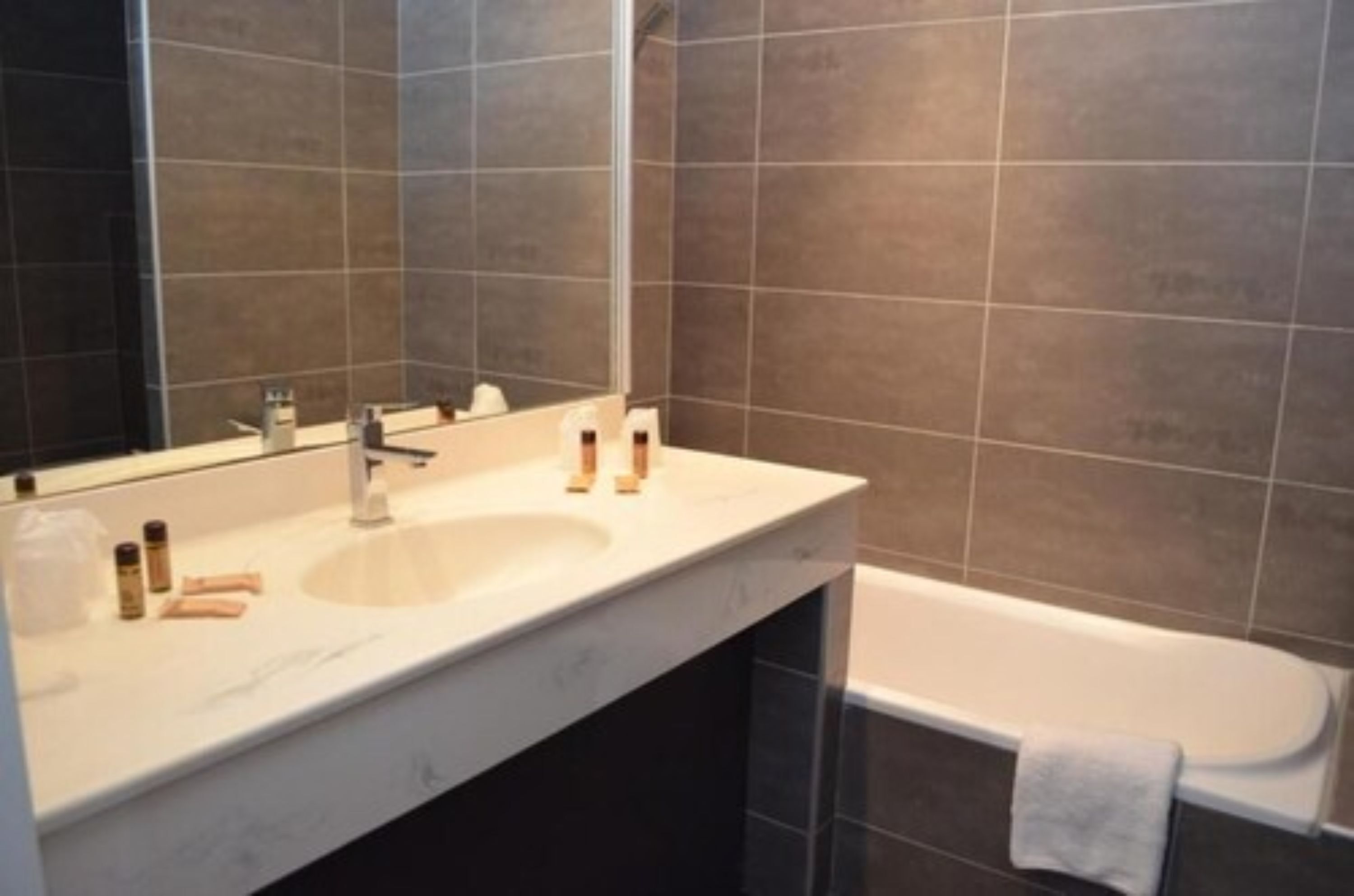 A modern bathroom with a large mirror, two sinks, and a bathtub.