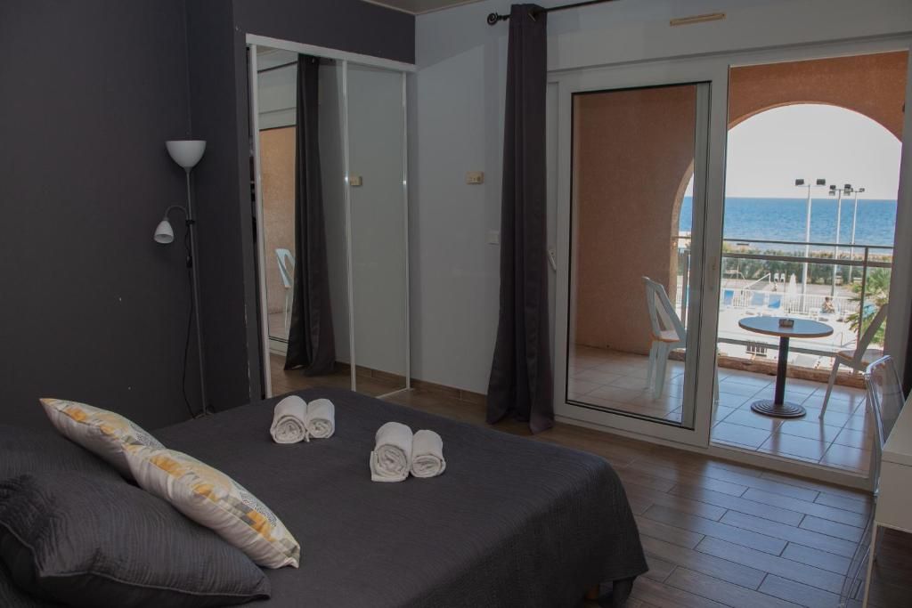 Une chambre d’hôtel avec un lit, une vue sur la mer et un balcon équipé d’une table et de chaises.