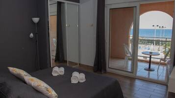 Ett hotellrum med en säng, utsikt över havet och en balkong med ett bord och stolar.