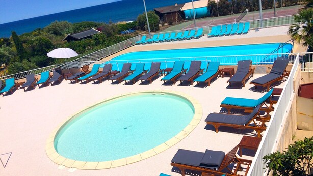 A pool area with sun loungers and a central swimming pool, surrounded by a fence and overlooking the ocean. - Hotel Orizonte (Cervione)