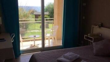 A hotel room with a bed, a desk, and a balcony with a view.