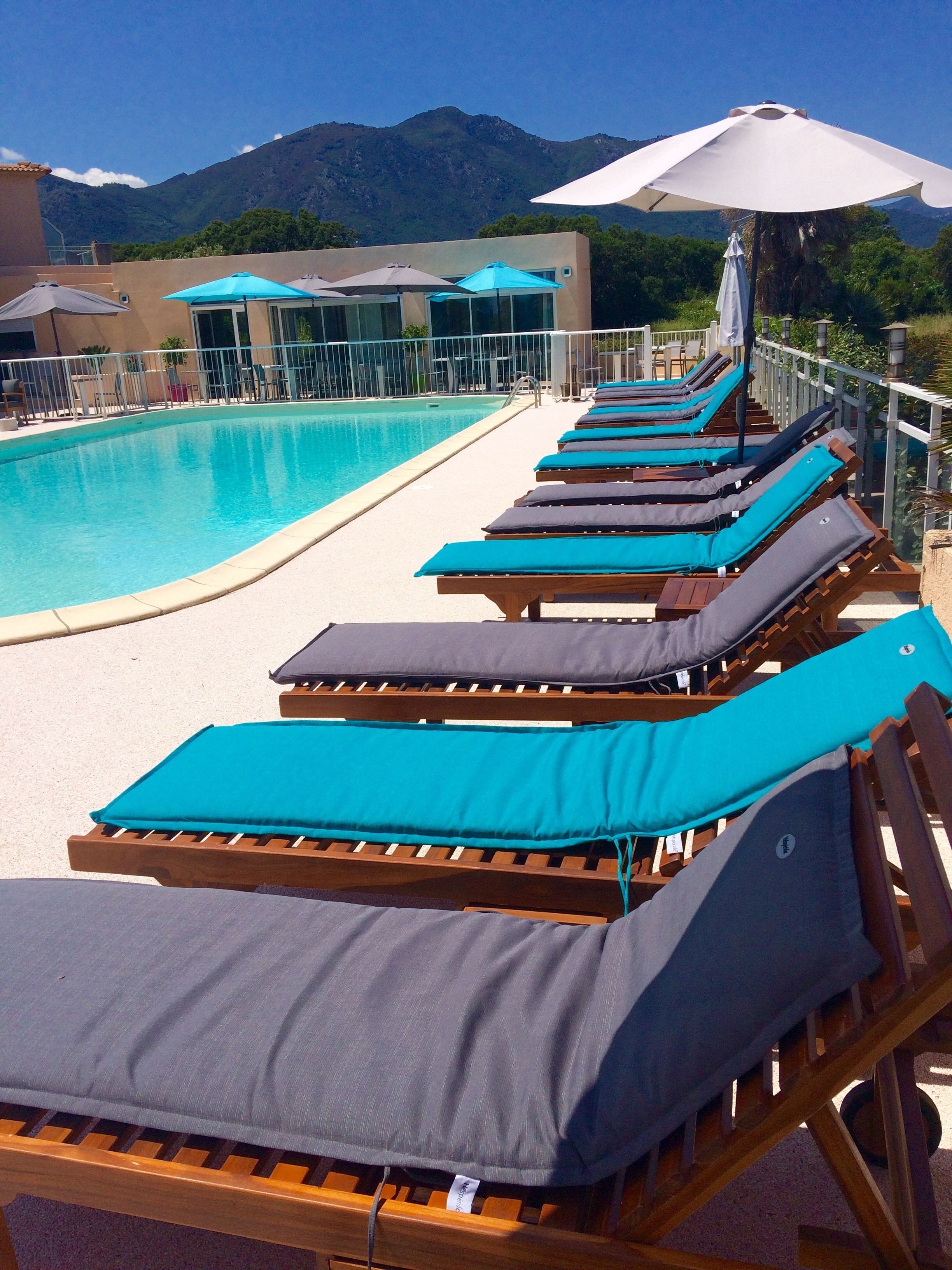 Un espace aménagé au bord de la piscine, avec des chaises longues et des parasols, une piscine à eau claire et des montagnes en arrière-plan.