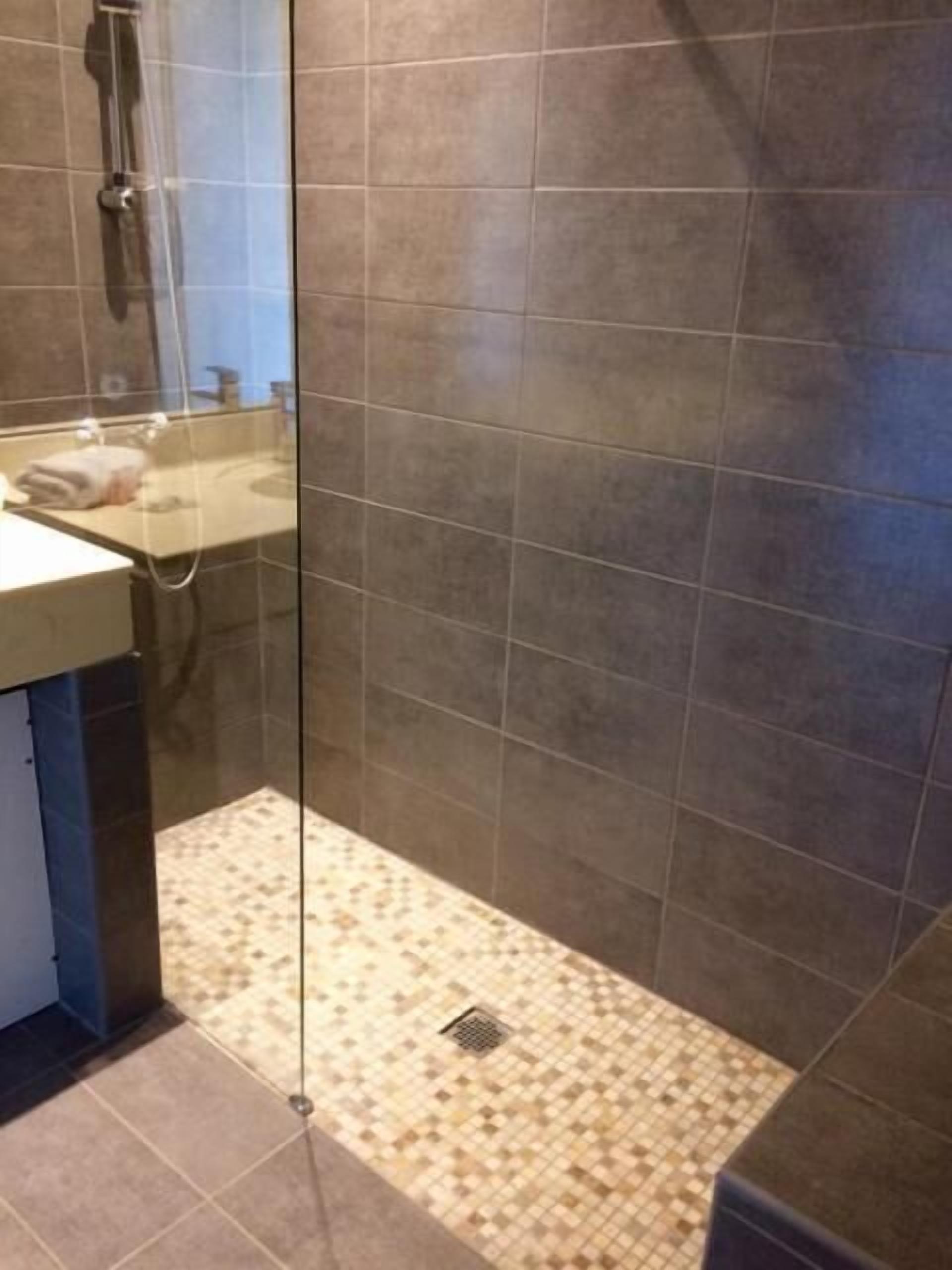 Un baño con zona de ducha, lavamanos y suelo de baldosas.
