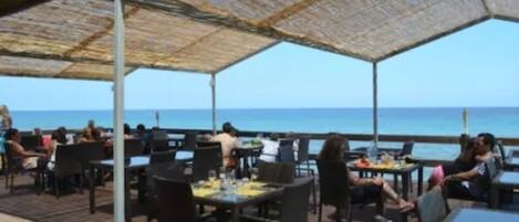 An outdoor dining area with tables and chairs, overlooking the sea.