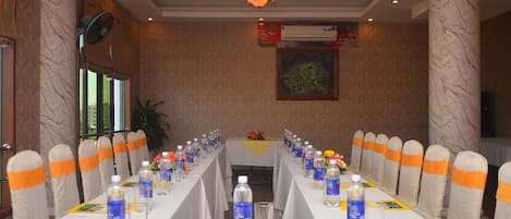 A conference room with a long table, chairs with orange sashes, water bottles, and a ceiling fan.