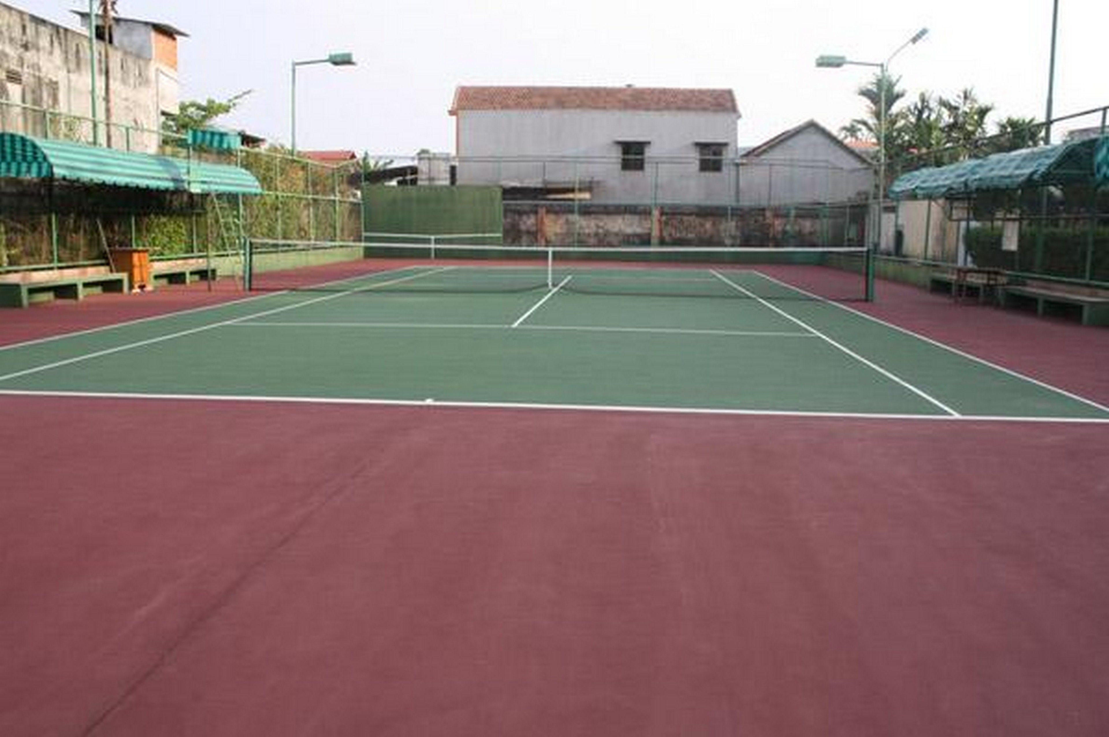 An outdoor tennis court with a red surface and green boundary lines.