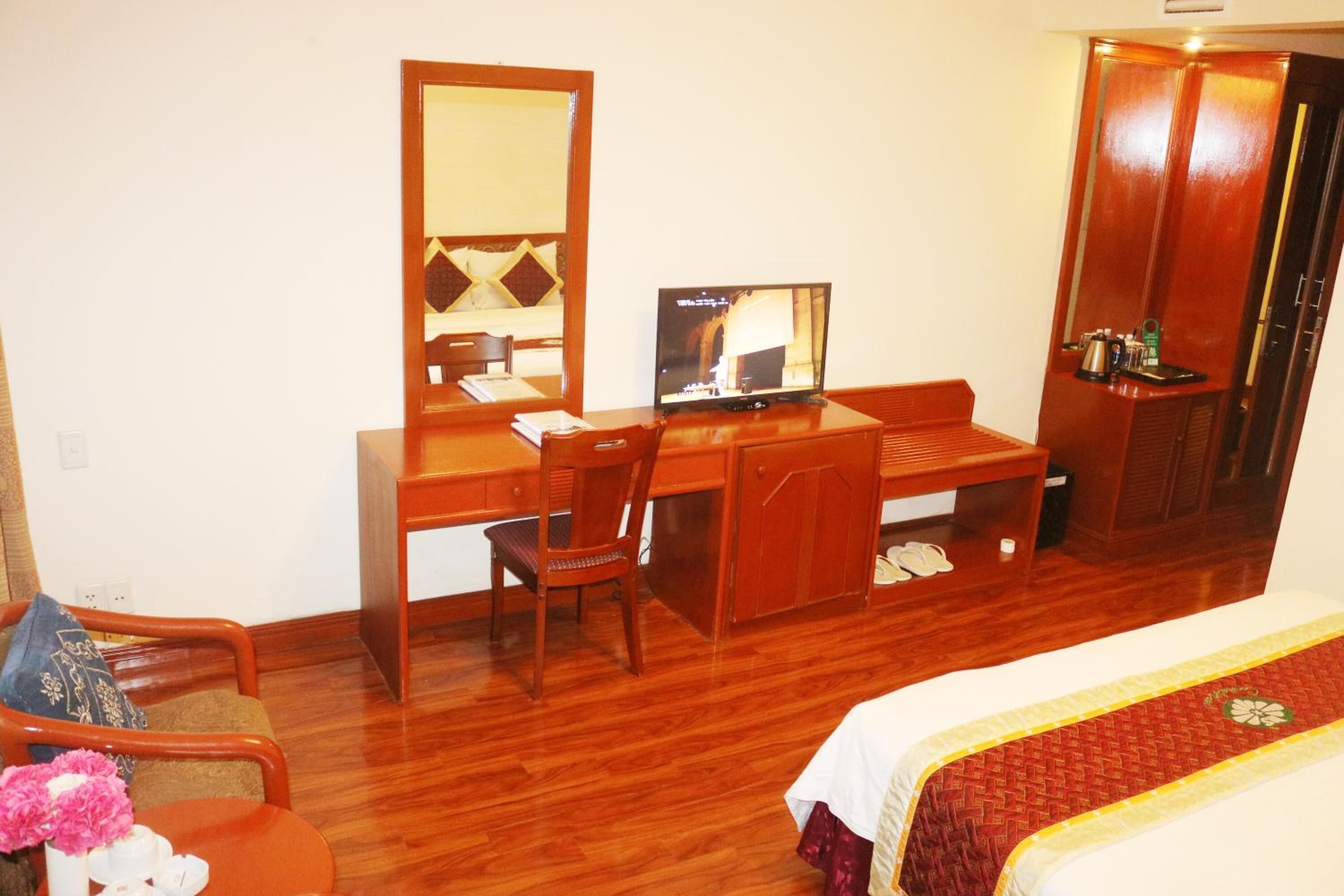 Habitación de hotel con un escritorio de madera, un televisor, un armario y una cama con colcha roja y blanca.