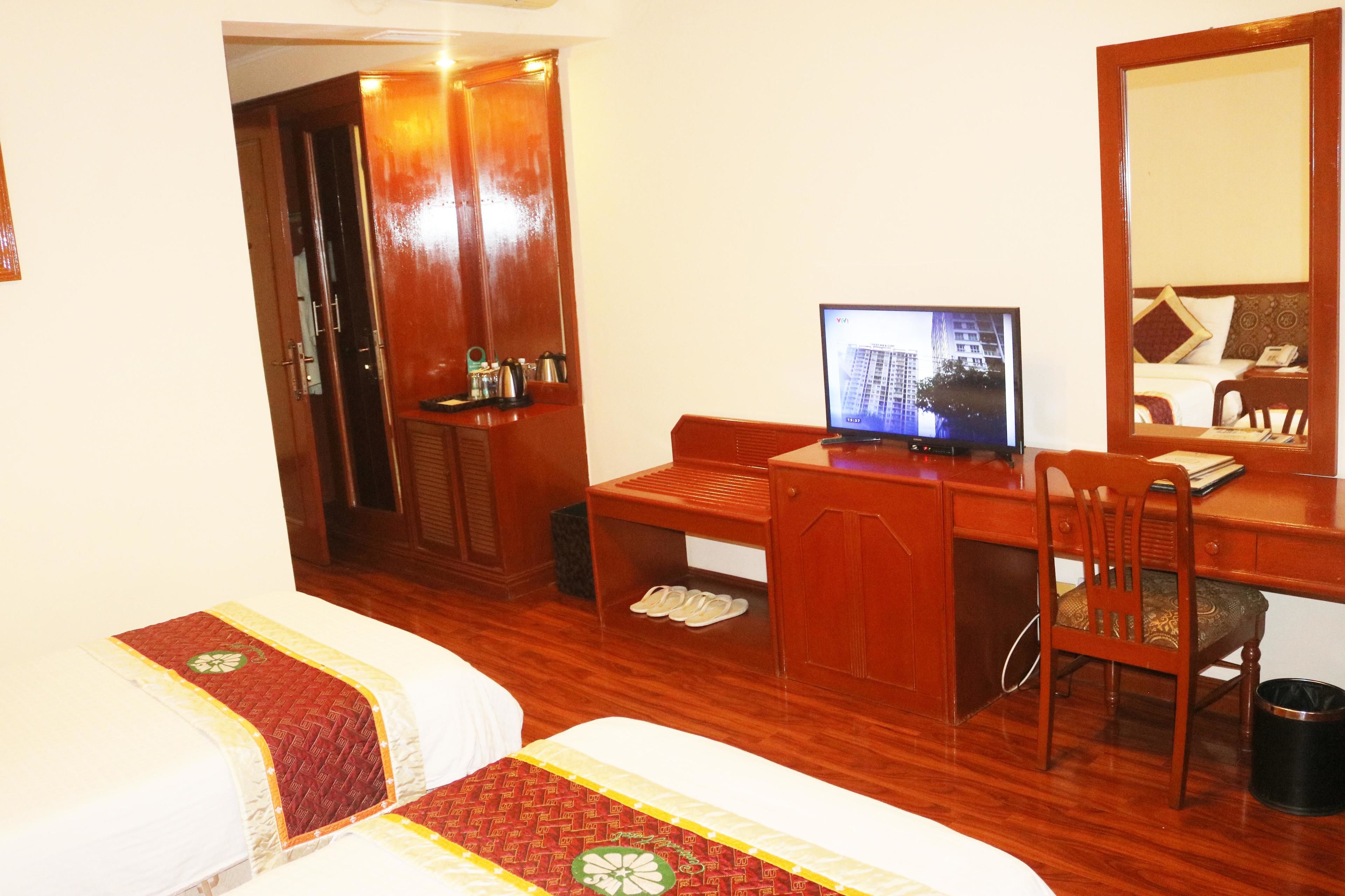 Une chambre d’hôtel avec deux lits, un bureau avec un ordinateur, une chaise, un miroir et une petite table avec un téléphone.