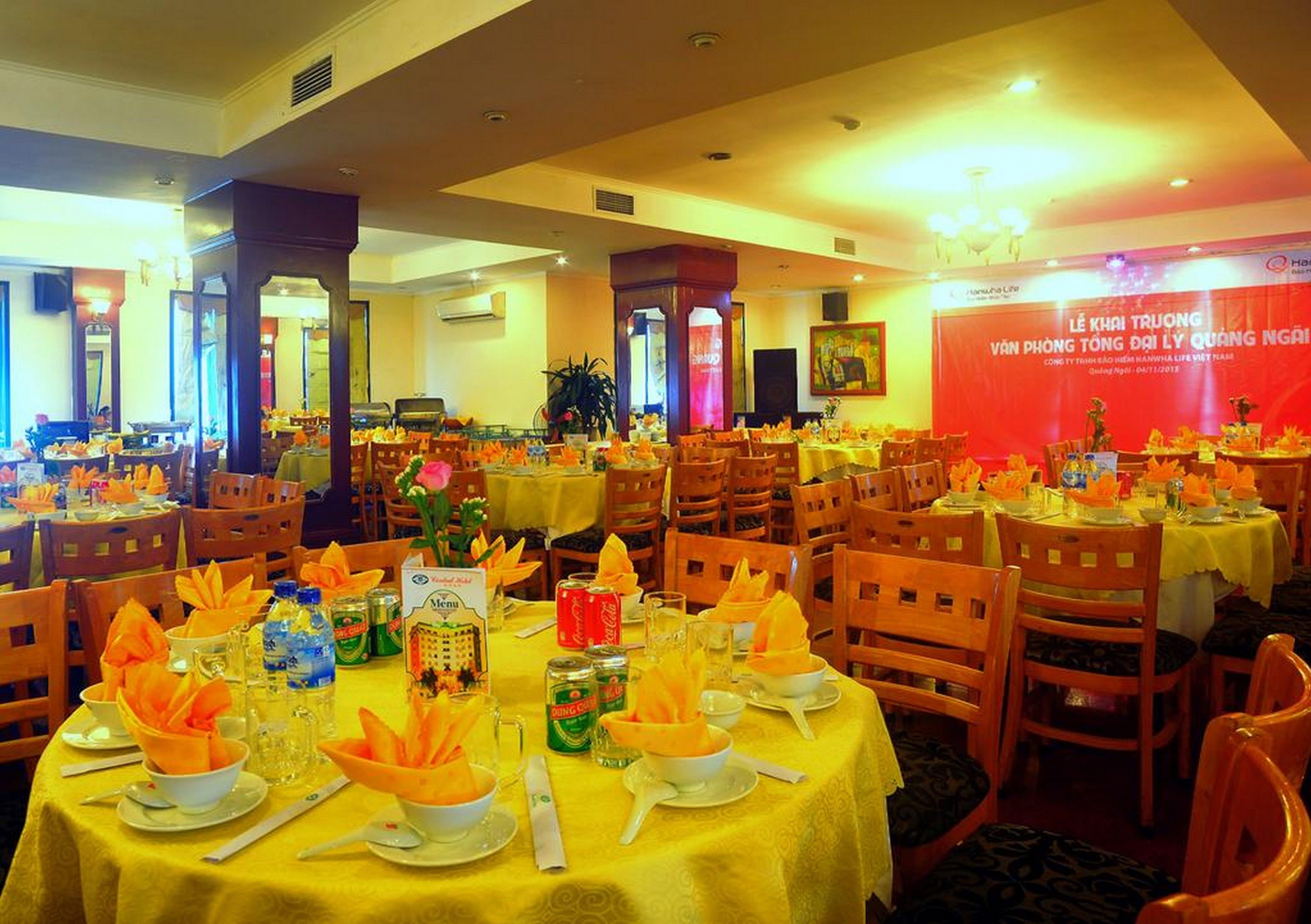 A banquet hall with round tables set for a formal event, featuring yellow tablecloths and orange napkin decorations.