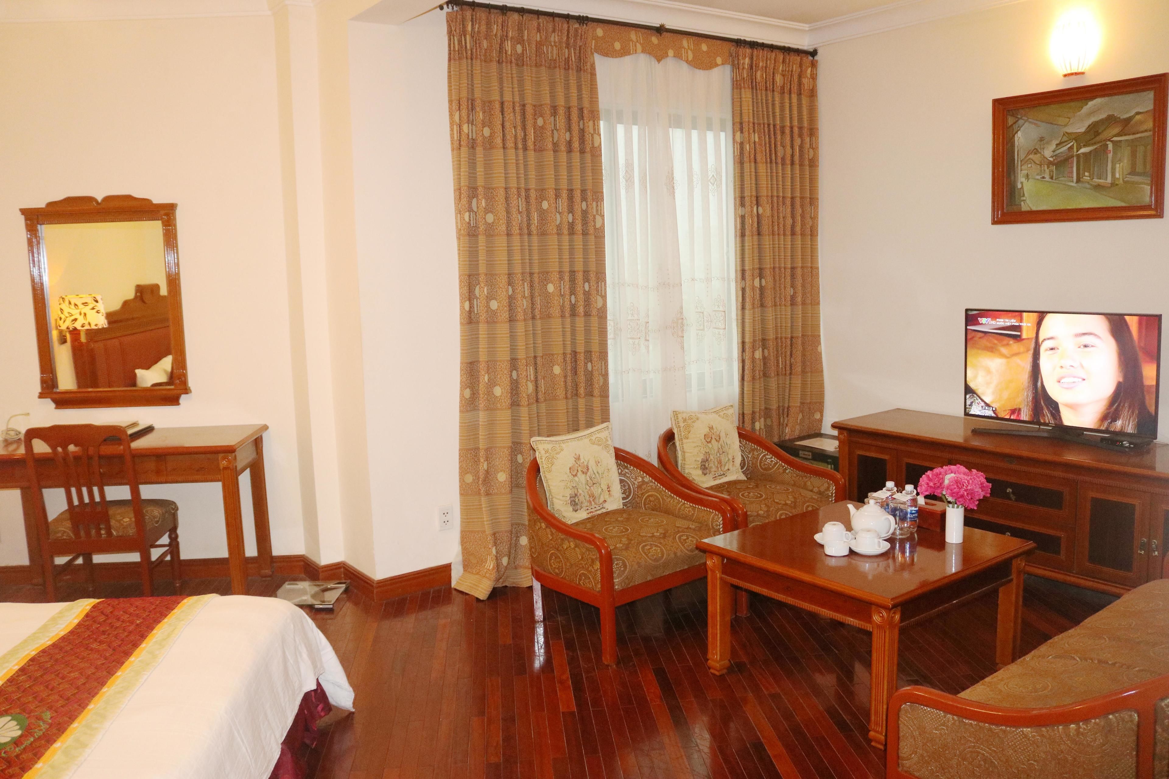 A hotel room with a bed, two armchairs, a small table, a television, and a mirror.