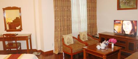 A hotel room with a bed, two armchairs, a small table, a television, and a mirror.