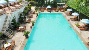 Piscina retangular com superfície de água azul cristalina, rodeada por áreas de estar ao ar livre com guarda-sóis e cadeiras.