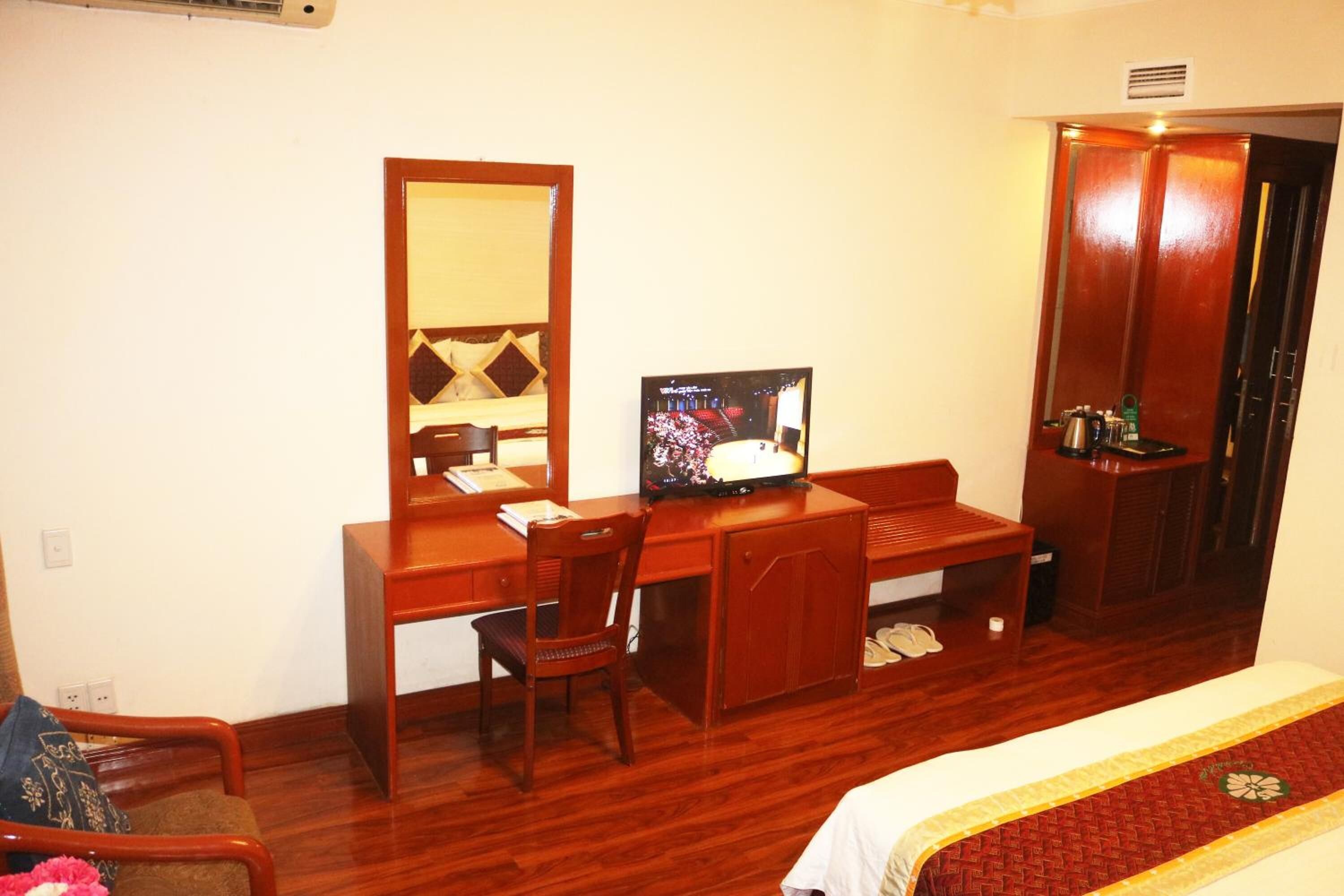 Een hotelkamer met een houten bureau, een televisie, een kledingkast en een bed met een rood-witte dekbedovertrek.
