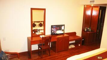 A hotel room with a wooden desk, a television, a wardrobe, and a bed with a red and white bedspread.