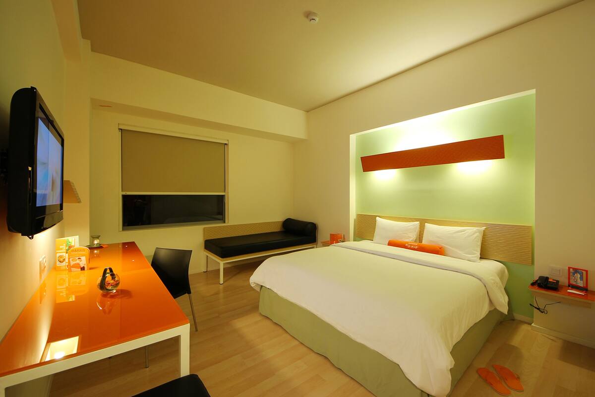 Una habitación de hotel moderna con una cama, un escritorio, una silla, un televisor y una ventana.