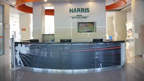 Un comptoir d’accueil d’hôtel orné d’une enseigne Harris, un écran numérique affichant un menu, et un design intérieur moderne.