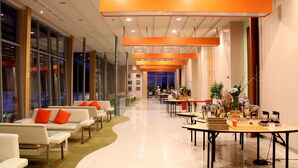Un hall d’hôtel moderne doté d’espaces détente, d’un comptoir d’accueil et d’un espace repas.