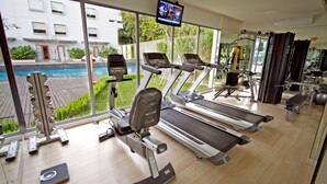 Une salle de sport équipée de tapis de course, d’appareils de musculation et d’un écran de télévision.