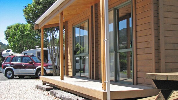 Un'accogliente baita moderna in legno con veranda coperta, ampie porte scorrevoli in vetro e vialetto sterrato.