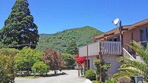 Un edificio residenziale con un balcone, circondato dal verde e con una montagna sullo sfondo.