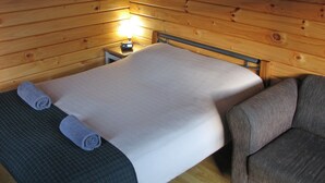 Una camera in una baita di legno, con un letto, una sedia e un comodino con una lampada.