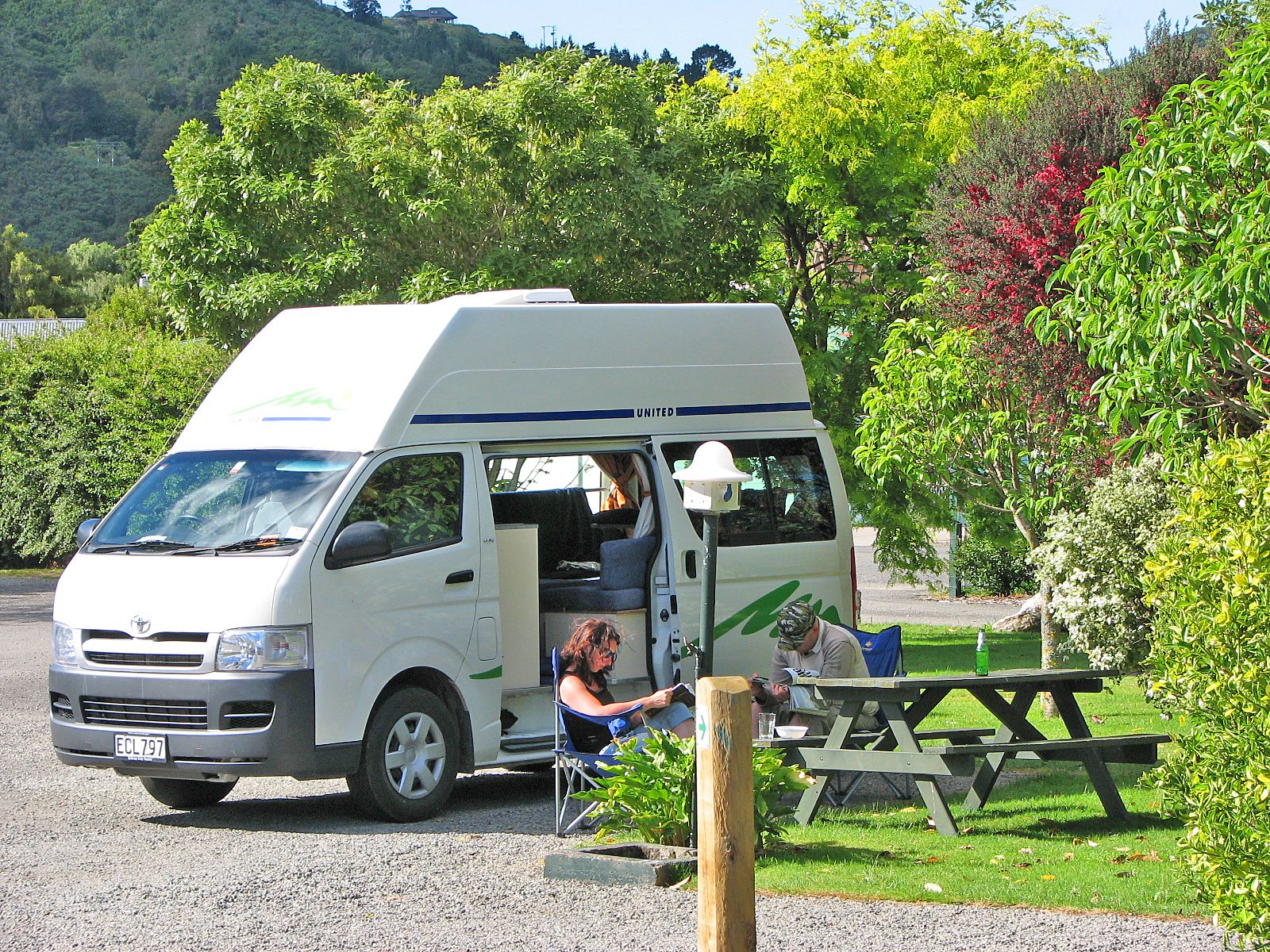 A white camper van parked in a park with a picnic table nearby.