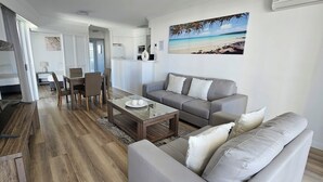 Ein modernes Wohnzimmer mit einem grauen Sofa, einem Couchtisch und einem Essbereich mit Tisch und Stühlen.