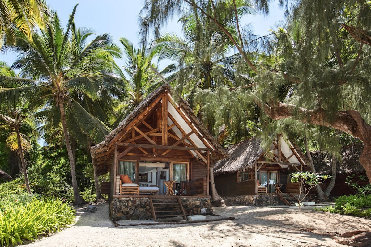 Ein Holzbungalow mit einem Reetdach, umgeben von Palmen und üppigem Grün.
