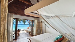 A bedroom with a bed, a chair, and a view of the beach. - Constance Tsarabanjina (Tsarabanjina)