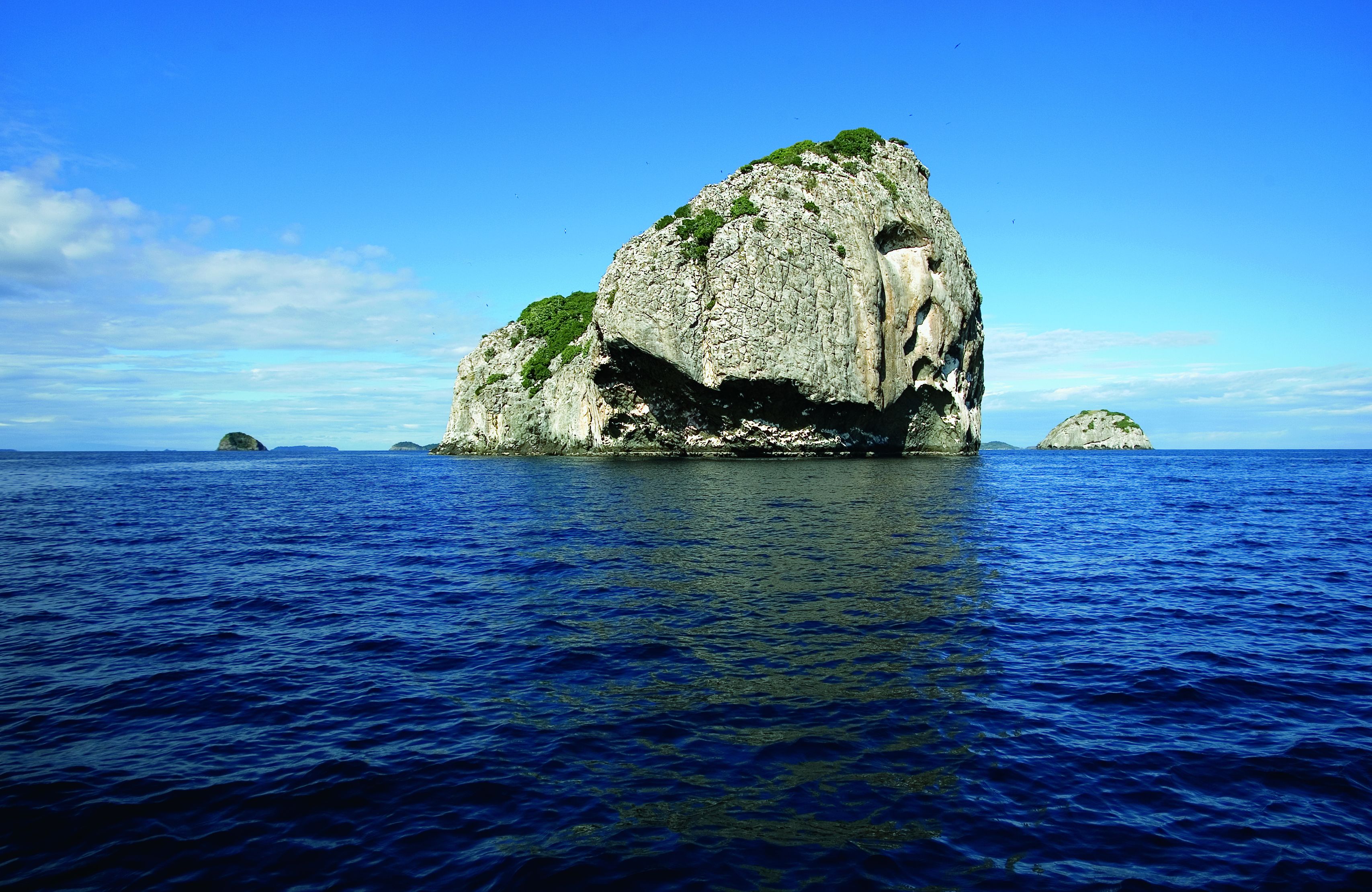 A large rock formation surrounded by clear blue water.