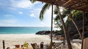 A wooden deck with lounge chairs and a small table, overlooking a beach with clear blue water and a rocky shoreline. - Constance Tsarabanjina (Tsarabanjina)