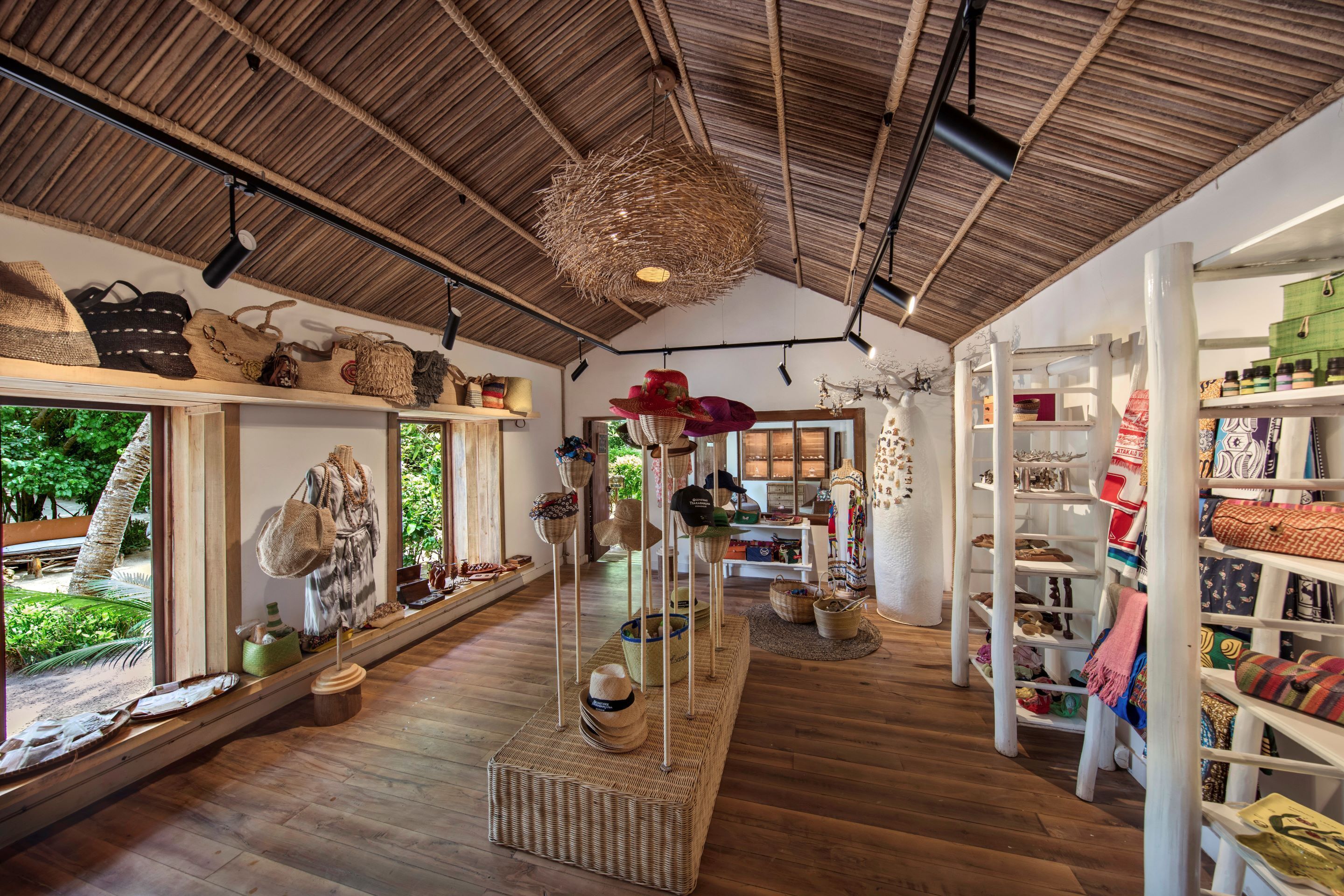 A boutique store with wooden flooring, wicker display stands, and shelves filled with hats and bags.
