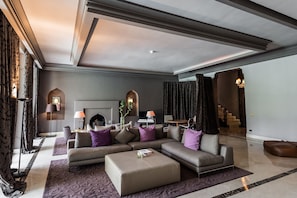 A modern living room with a sectional sofa, a coffee table, and a fireplace. There are decorative lamps and a staircase in the background.