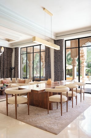 A spacious living area with a large wooden coffee table surrounded by chairs, a sofa, and a chandelier.