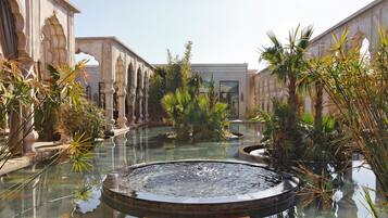 A courtyard with a central water feature, surrounded by palm trees and stone pathways.