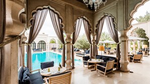 An outdoor seating area with tables and chairs, overlooking a pool. - Palais Namaskar (Marrakech)