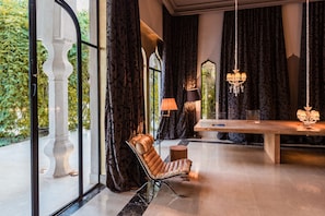 A modern interior with a large glass door, a cushioned chair, a wooden table, and a chandelier. - Palais Namaskar (Marrakech)