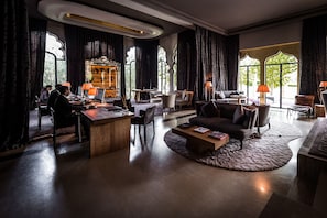 A spacious hotel lobby with a reception desk, seating area, and large windows offering views of the outdoors.