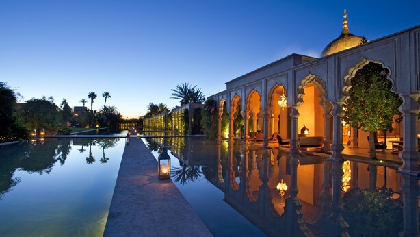 A serene pool area with a reflection of the building and palm trees, surrounded by ornate architecture and warm lighting. - Palais Namaskar (Marrakech)