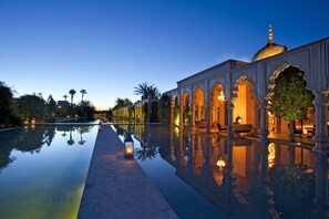 A serene pool area with a reflection of the building and palm trees, surrounded by ornate architecture and warm lighting. - Palais Namaskar (Marrakech)