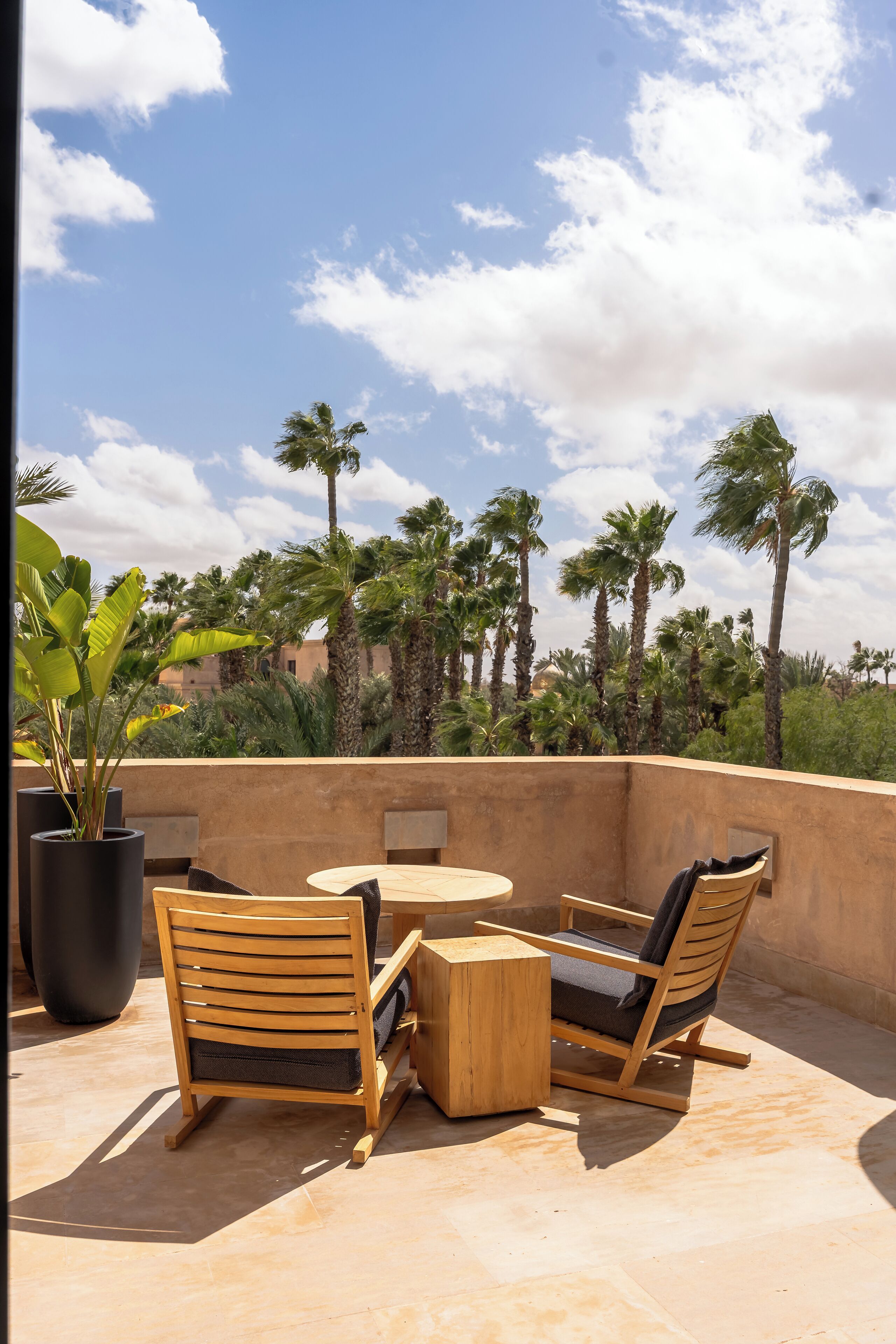 Une terrasse dotée de mobilier en bois et offrant une vue sur des palmiers et des immeubles.