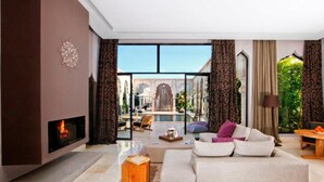 A modern living room with a fireplace, a sofa, a coffee table, and a view of a pool and outdoor area. - Palais Namaskar (Marrakech)