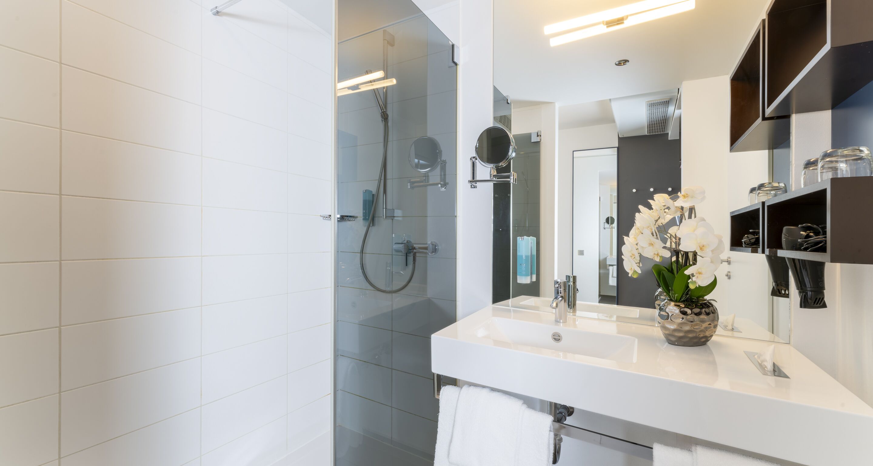 Un baño moderno con cabina de ducha de vidrio, un lavabo blanco y un espejo con un florero.
