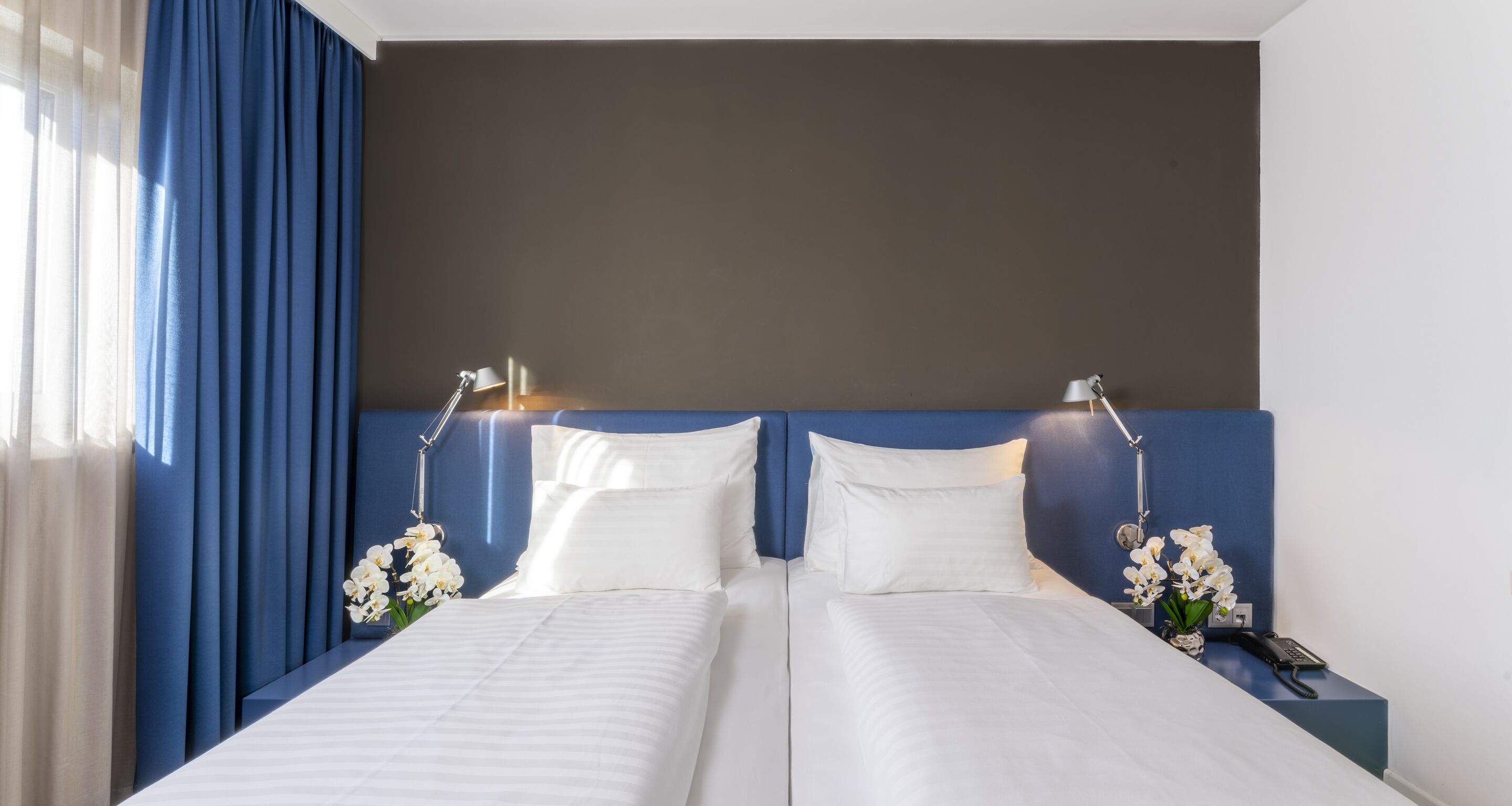 A double bed with white linens, two bedside lamps, a nightstand with a phone, and white orchids.
