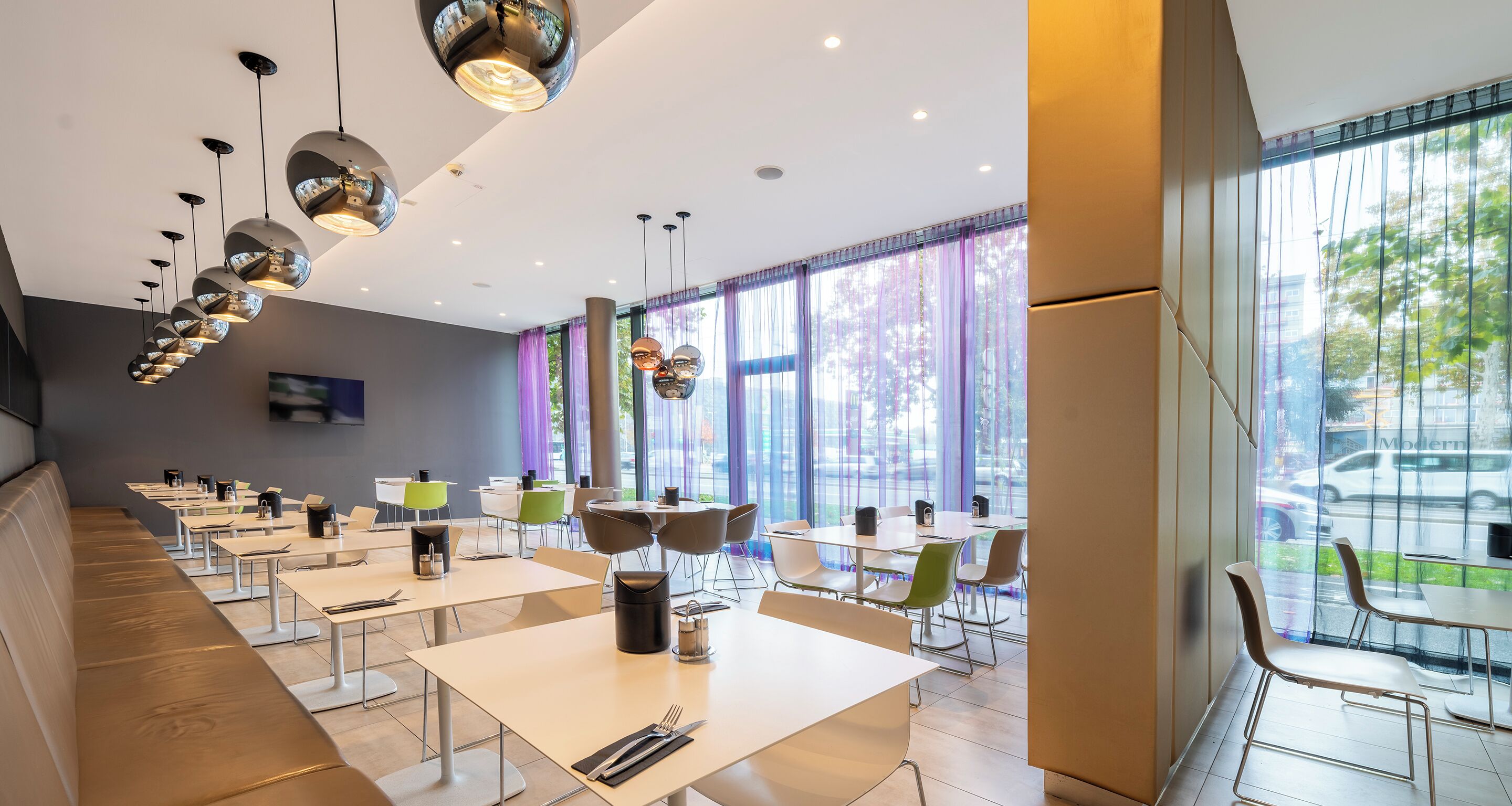 Een modern restaurant met lange gedeelde tafels, afzonderlijke zitjes en hangende lampen.