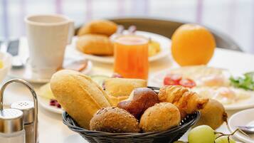 A breakfast table with bread, pastries, and a fruit bowl.