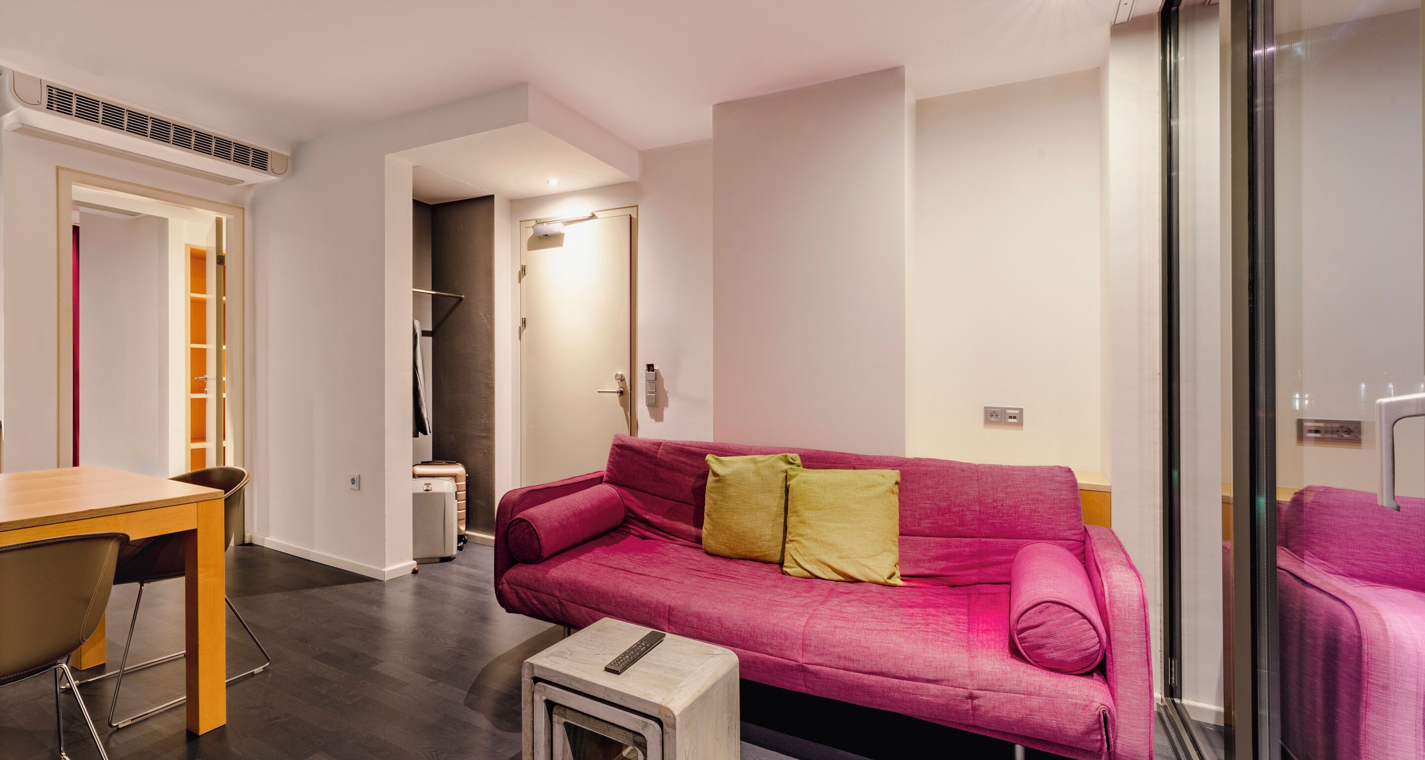 Una sala de estar moderna con una mesa de madera, un sofá rosa con cojines y una pequeña mesita blanca con un control remoto.